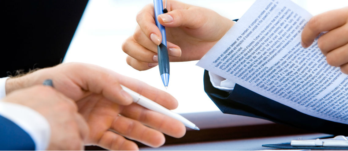 two people hold pens over a medical plan contract as they discuss renewing insurance
